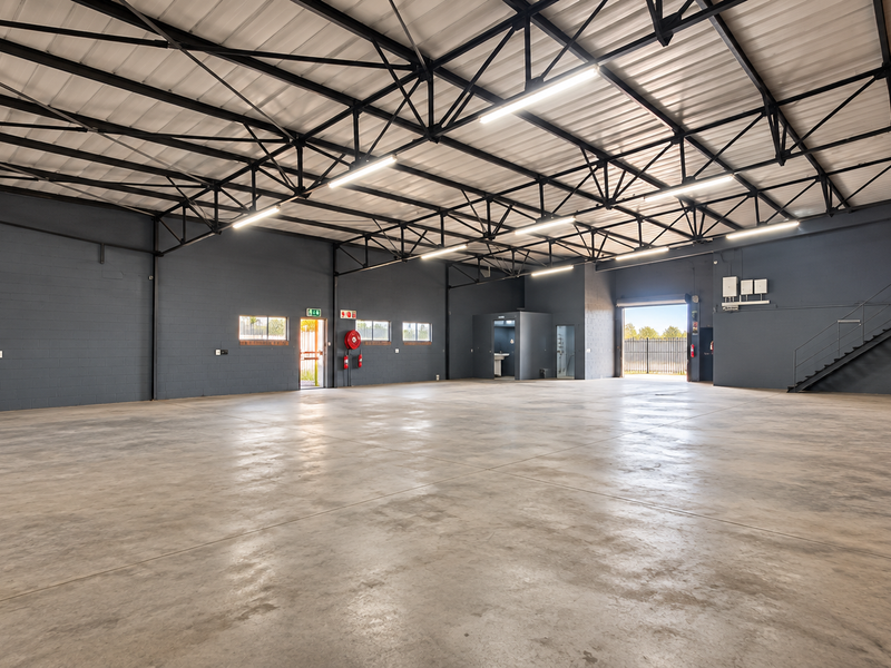 Spacious industrial warehouse featuring high ceilings with exposed steel trusses, polished concrete flooring, and a functional mezzanine staircase.