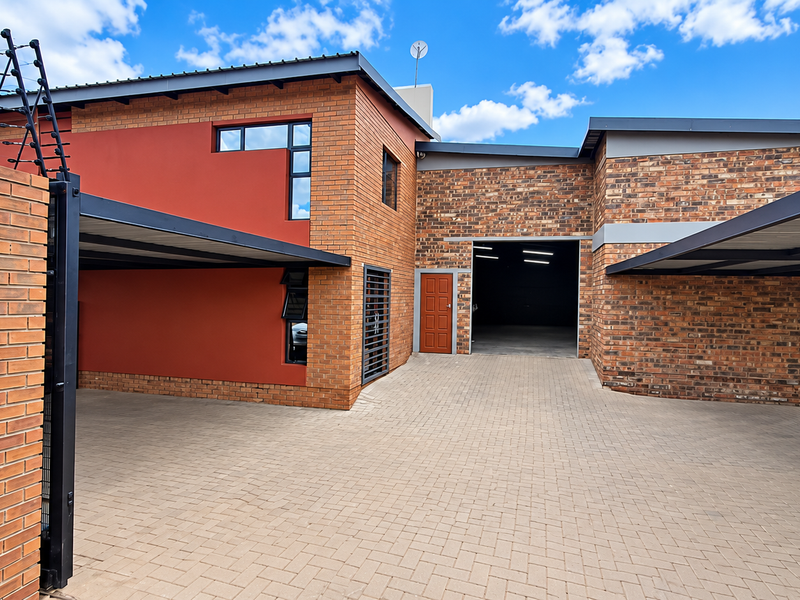 Modern industrial property featuring a brick facade, paved driveway, multiple carports, and secure perimeter fencing with an industrial roller door entrance.