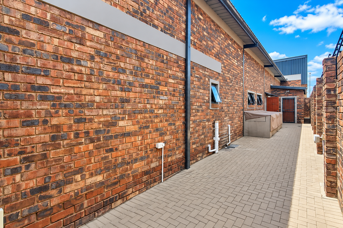 A well-maintained exterior side passage featuring face brick walls, paved flooring, and secure perimeter electric fencing.