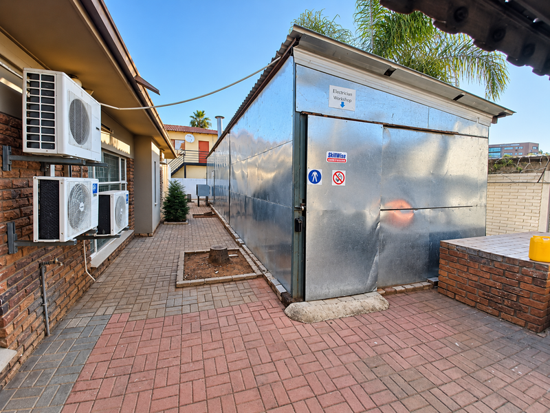 Exterior rear view of the office property featuring a paved walkway, brick walling, and a metal-clad workshop structure with mounted air conditioning units.