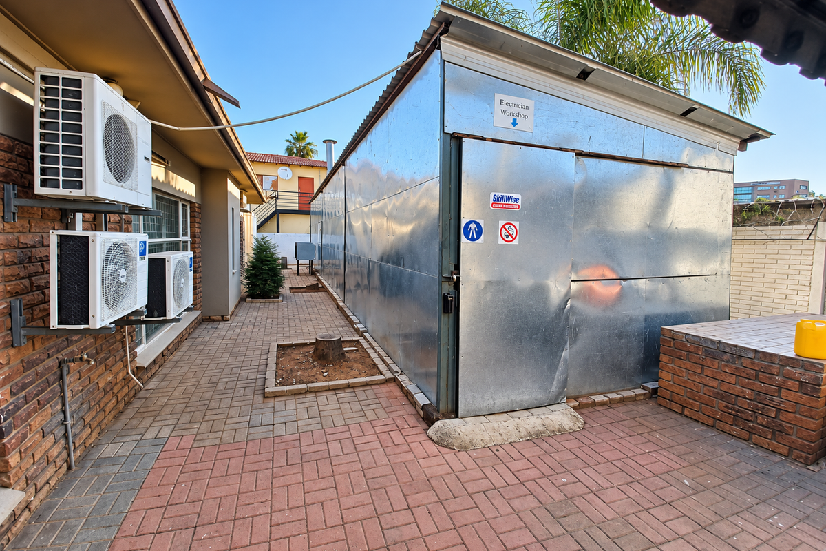Exterior rear view of the office property featuring a paved walkway, brick walling, and a metal-clad workshop structure with mounted air conditioning units.