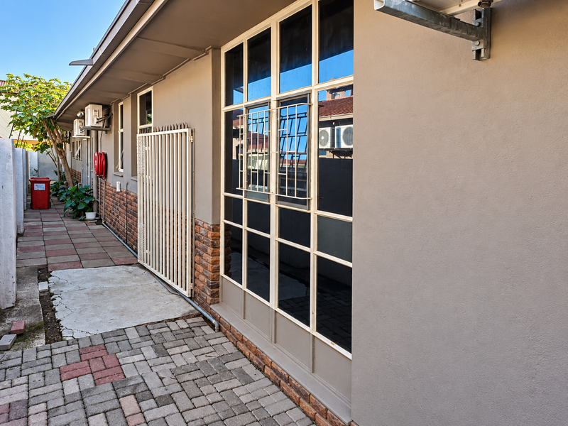 A side exterior view of the office building featuring paved walkways, large glass windows, and security infrastructure.
