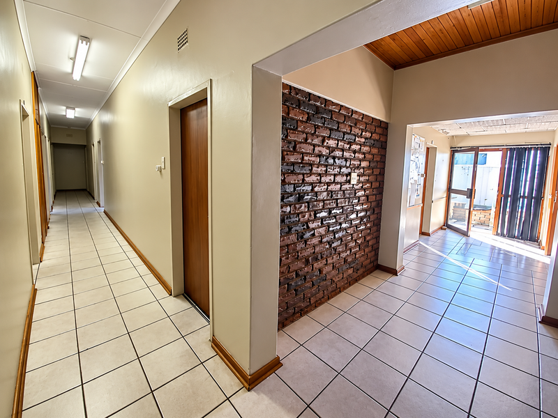 Spacious office hallway featuring ceramic tile flooring, an exposed brick feature wall, and timber ceiling accents, leading to an exterior entrance.