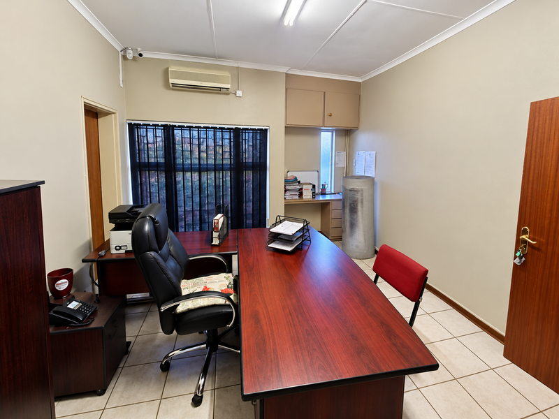A functional office space featuring tiled flooring, built-in cabinetry, a split-system air conditioner, and security bars on the window.