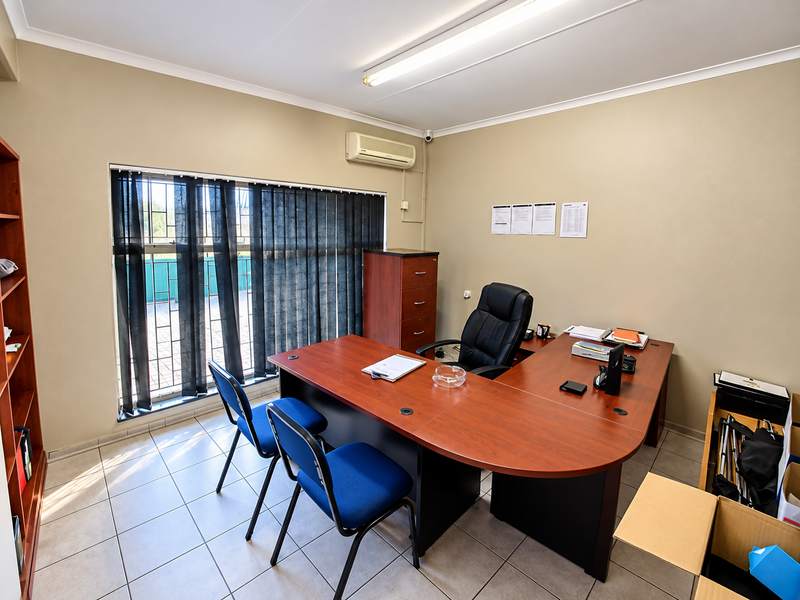 A functional office space featuring tiled flooring, an air conditioning unit, and a large window with security bars.