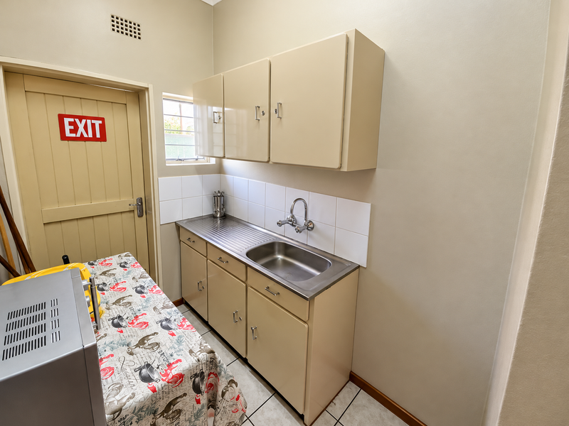 A functional scullery area featuring built-in cabinetry, a stainless steel sink, tiled backsplash, and tiled flooring, providing practical utility space.