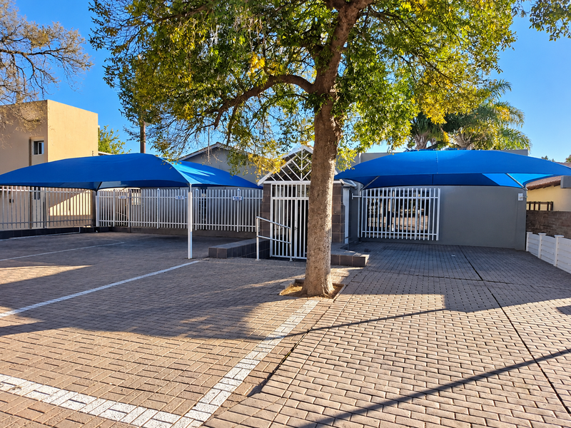 Front exterior view of the office property featuring a paved parking area with blue shade cloth carports and secure perimeter fencing.