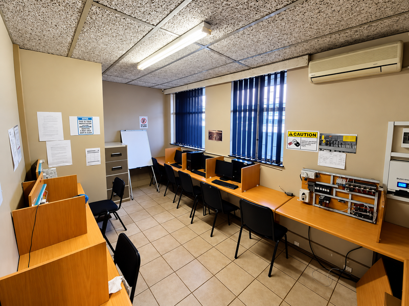 A functional office space featuring built-in desk workstations, acoustic ceiling tiles, tiled flooring, and a wall-mounted split-system air conditioning unit.