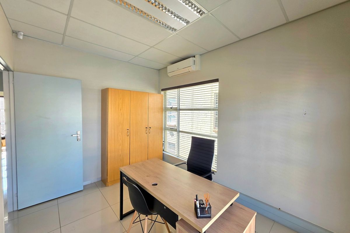 A functional office space featuring tiled flooring, a suspended ceiling with integrated lighting, a wall-mounted air conditioning unit, and built-in storage cabinetry.