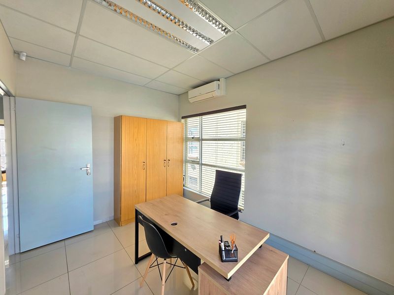 A functional office space featuring tiled flooring, a suspended ceiling with integrated lighting, a wall-mounted air conditioning unit, and built-in storage cabinetry.