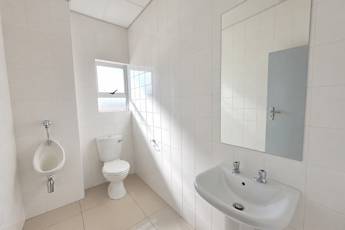 A clean, functional office bathroom featuring a pedestal basin, toilet, wall-mounted urinal, and full-height wall tiling.