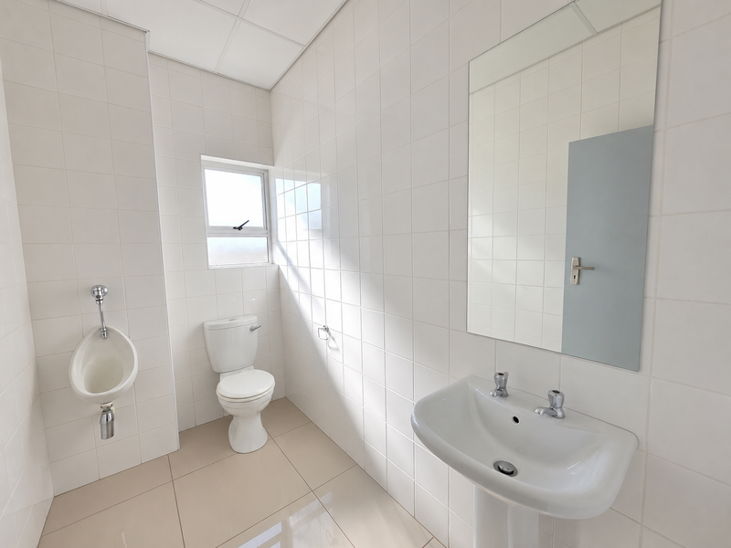 A clean, functional office bathroom featuring a pedestal basin, toilet, wall-mounted urinal, and full-height wall tiling.