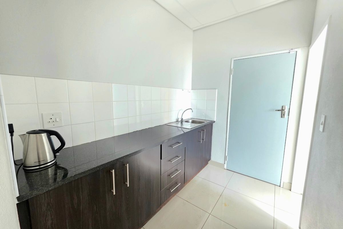 A clean, functional office kitchenette featuring dark wood cabinetry, granite countertops, a stainless steel sink, and white tiled backsplash.