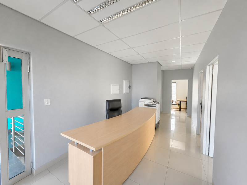 A professional office reception area featuring tiled flooring, a suspended ceiling with recessed lighting, and clean neutral wall finishes.
