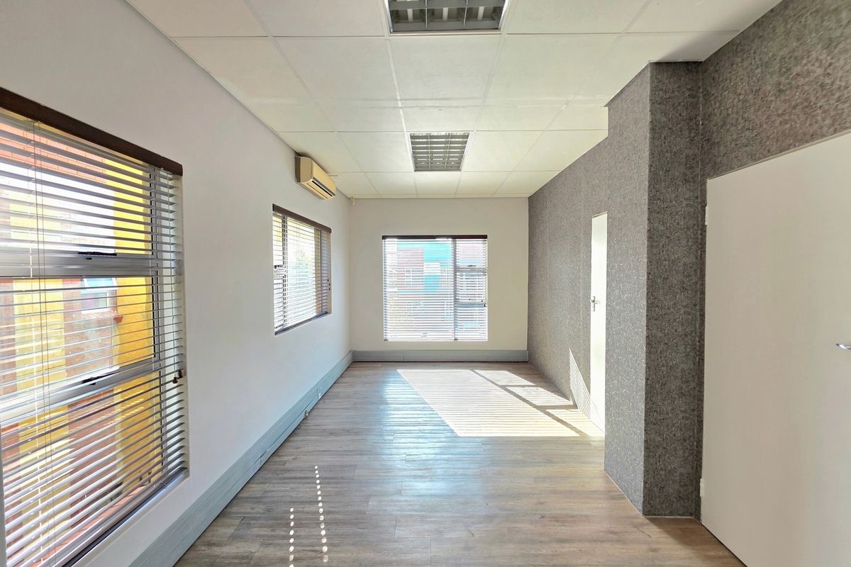 A bright, empty office space featuring laminate flooring, a textured feature wall, suspended ceiling with recessed lighting, and split-system air conditioning.
