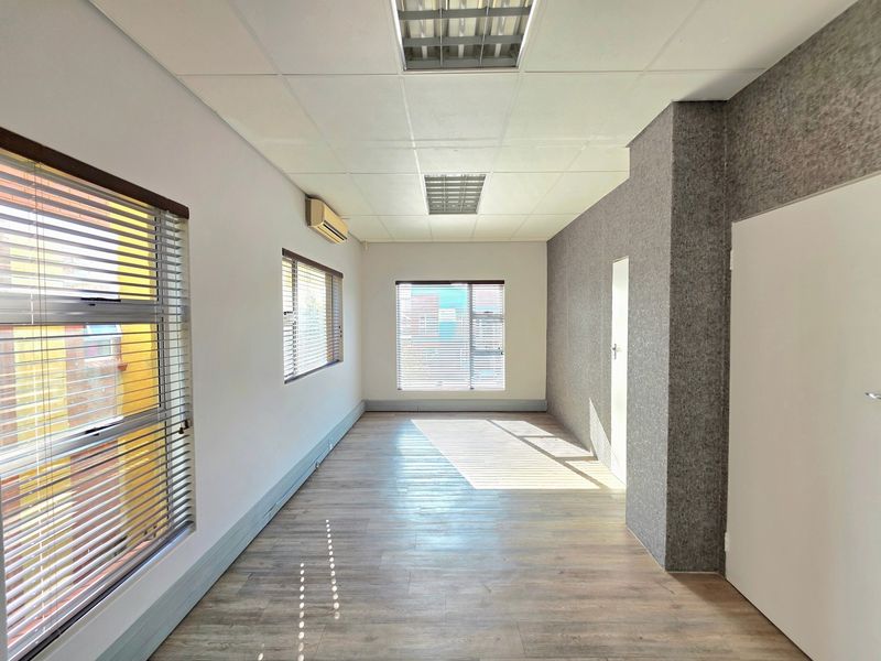 A bright, empty office space featuring laminate flooring, a textured feature wall, suspended ceiling with recessed lighting, and split-system air conditioning.