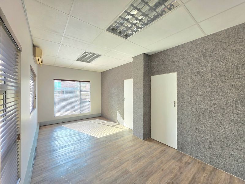A bright, empty office space featuring laminate flooring, acoustic wall paneling, recessed ceiling lighting, and a wall-mounted air conditioning unit.