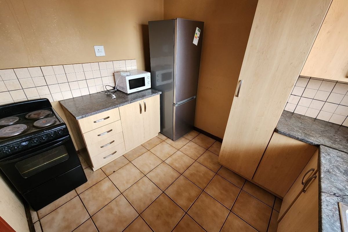 A functional kitchen featuring laminate cabinetry, stone-look countertops, ceramic tile backsplash, and tiled flooring, equipped with a freestanding electric stove.