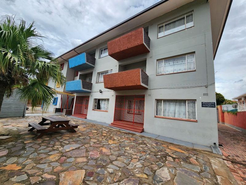 Rear view of a multi-story apartment building featuring balconies, security gates, and stone-paved outdoor area.