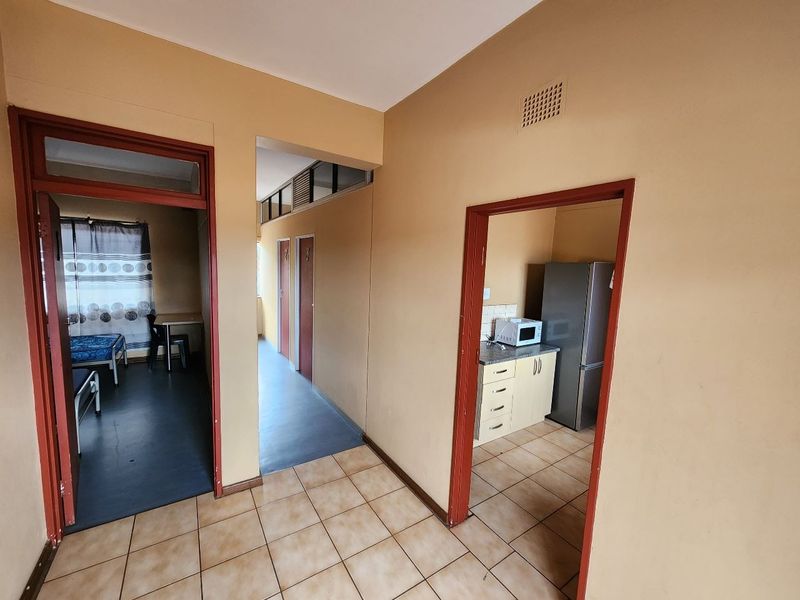 A view from the hallway looking into a bedroom and a small kitchen area featuring tiled floors and basic built-in cabinetry.
