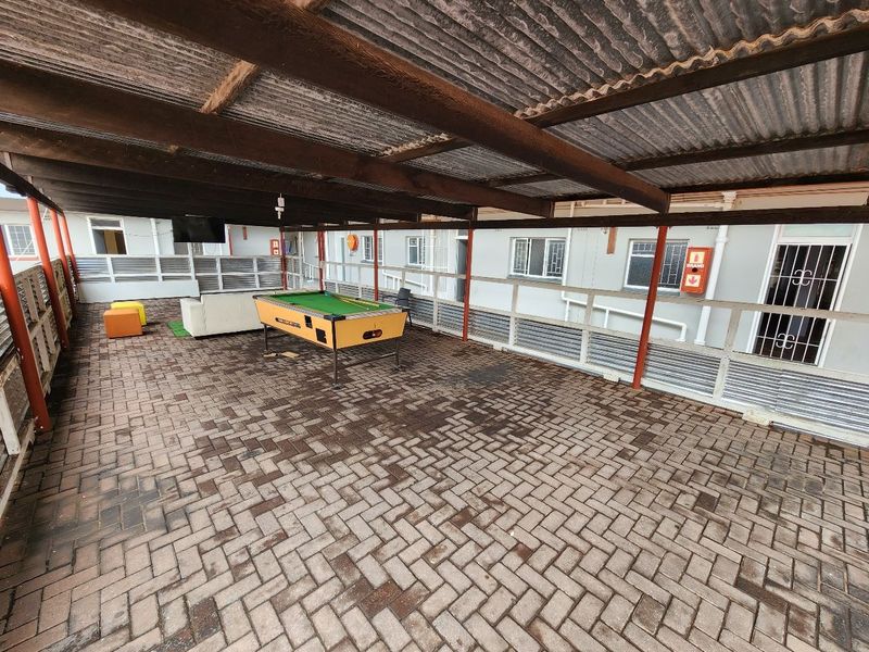 A large covered outdoor patio area featuring paved flooring, a corrugated iron roof with timber supports, and a metal safety balustrade.