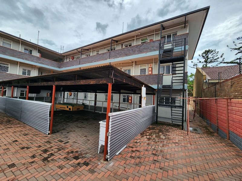 Rear view of the apartment complex featuring a covered parking area, external metal staircase, and brick-paved courtyard.