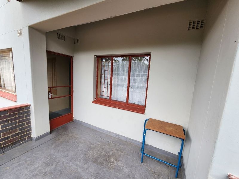 A covered balcony area featuring concrete flooring, metal-framed windows with security bars, and a secure entrance door.
