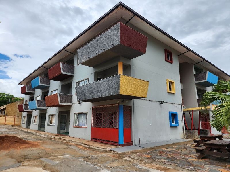 Exterior view of a multi-story apartment building featuring distinctive cantilevered balconies with colorful accents and ground-level security gates.