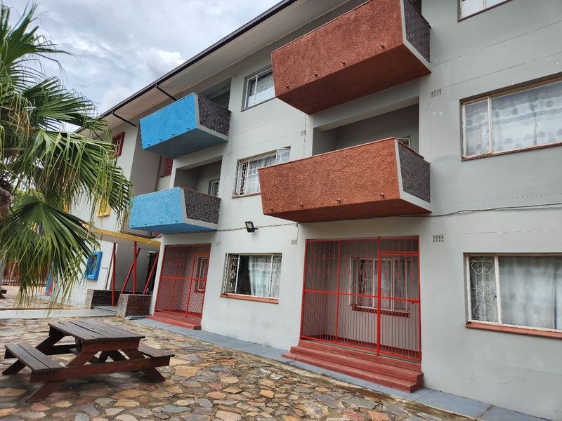 Exterior view of an apartment building featuring multiple balconies, security gates on ground floor units, and a paved courtyard area.