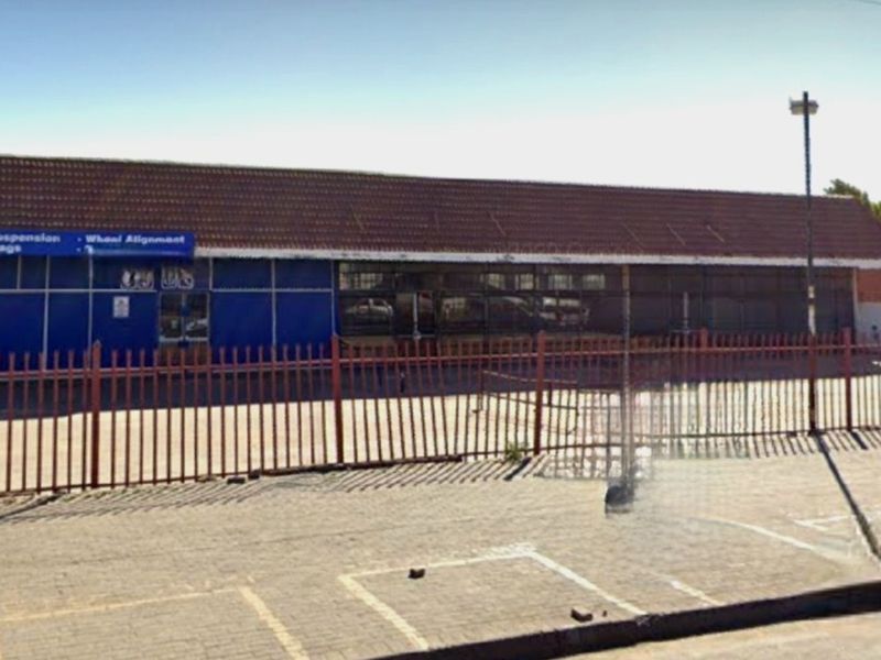 Commercial street-front property featuring a large glass facade, tiled roof, and secure perimeter fencing with an adjacent paved parking area.