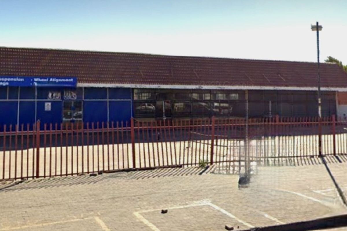 Commercial property exterior featuring a tiled roof, large glass storefront windows, and a paved parking area secured by metal fencing.