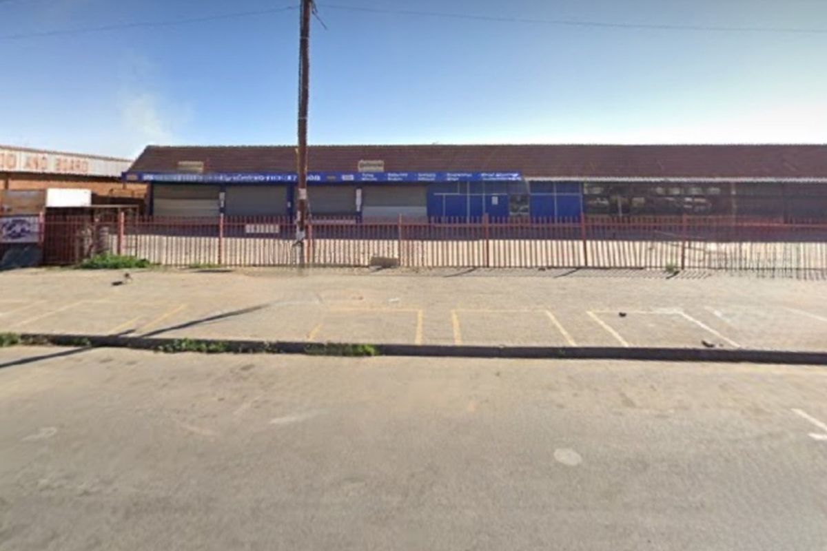 Commercial property frontage featuring a paved parking area, security fencing, and multiple roller shutter doors under a tiled roof.