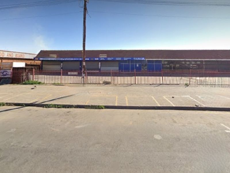 Commercial property frontage featuring a paved parking area, security fencing, and multiple roller shutter doors under a tiled roof.