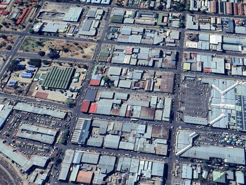 An aerial view of a dense commercial and industrial district featuring various warehouse structures, road networks, and large parking facilities.