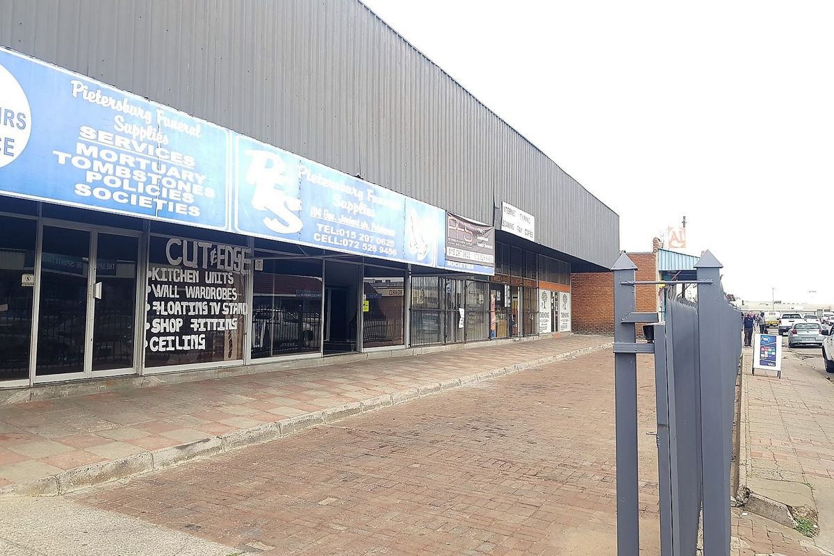 Front exterior view of a commercial building featuring metal cladding, large glass storefronts, and brick paved frontage.
