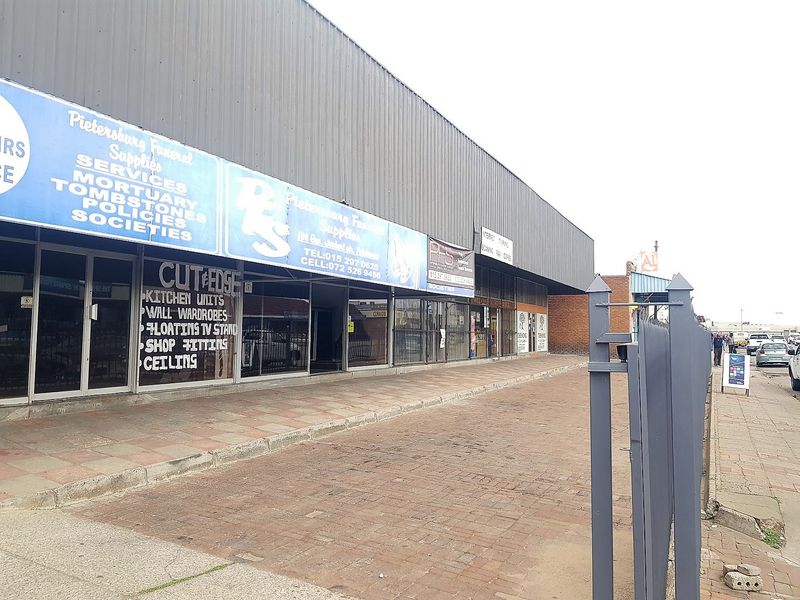 Front exterior view of a commercial building featuring metal cladding, large glass storefronts, and brick paved frontage.
