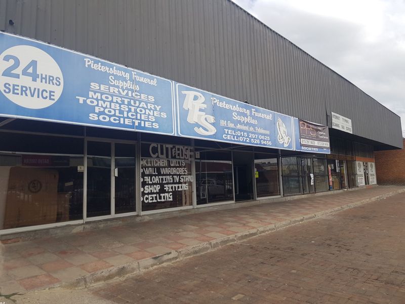 Commercial street-level storefront featuring large glass display windows, metal cladding, and prominent business signage along a paved sidewalk.