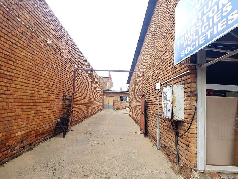 A narrow exterior alleyway between two commercial brick buildings featuring a concrete driveway and an exposed electrical distribution box.