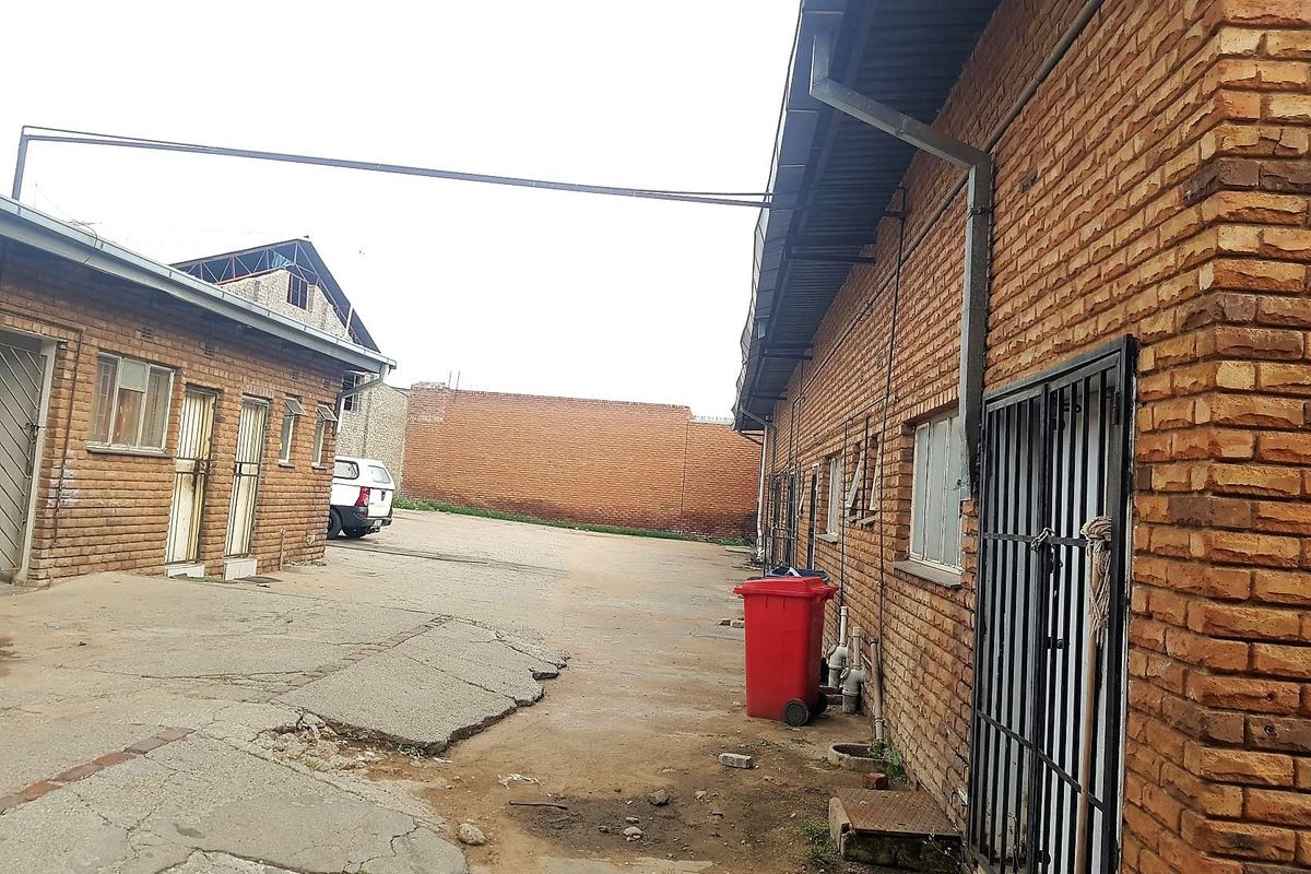 Rear exterior view of a commercial property featuring exposed brick walls, metal security gates, and a concrete paved yard area.