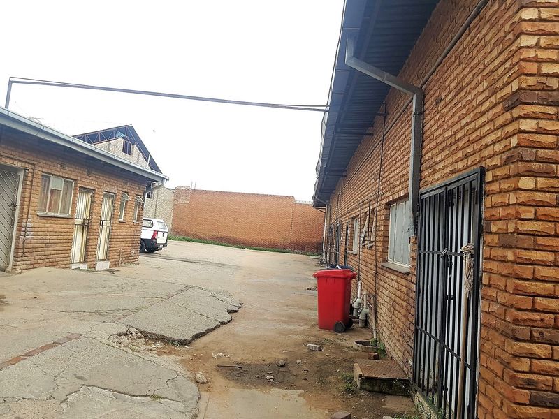 Rear exterior view of a commercial property featuring exposed brick walls, metal security gates, and a concrete paved yard area.