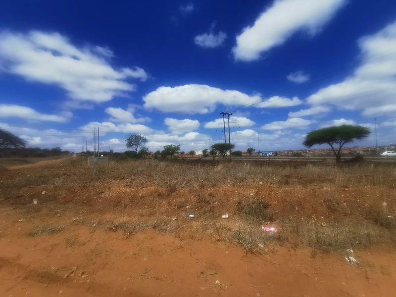 A view of a vacant commercial land plot featuring natural terrain, utility poles, and overhead power lines with road access.