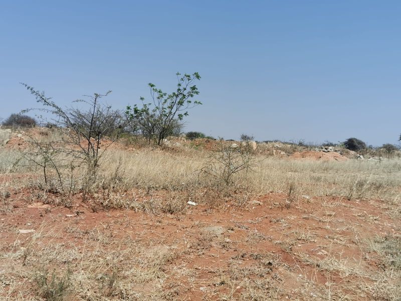 A view of a vacant commercial land plot featuring natural terrain and sparse vegetation under a clear sky.