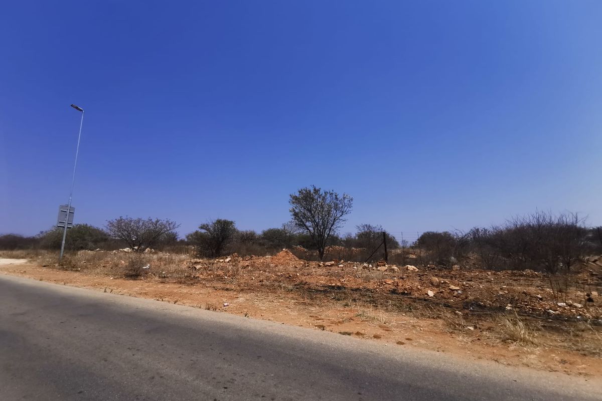 A street-level view of the vacant commercial land, showing the adjacent asphalt road, street lighting, and natural terrain.