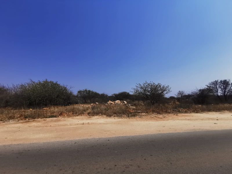 A view of the vacant commercial land plot from the adjacent asphalt road, featuring natural terrain and native vegetation.