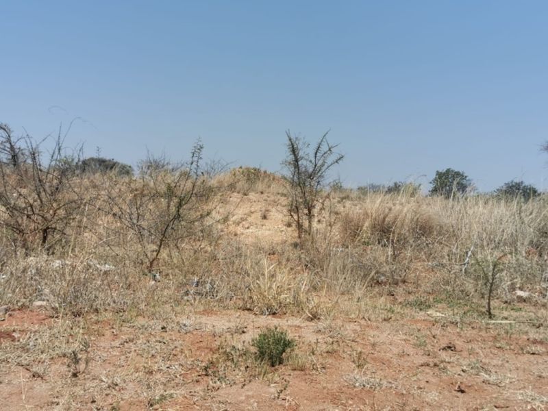 A view of undeveloped vacant land featuring natural dry vegetation and uneven terrain under a clear blue sky.