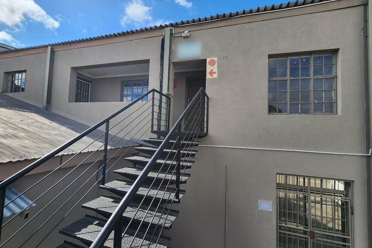 Rear exterior view of a commercial building featuring a metal staircase, security grilles on windows, and fire safety signage.