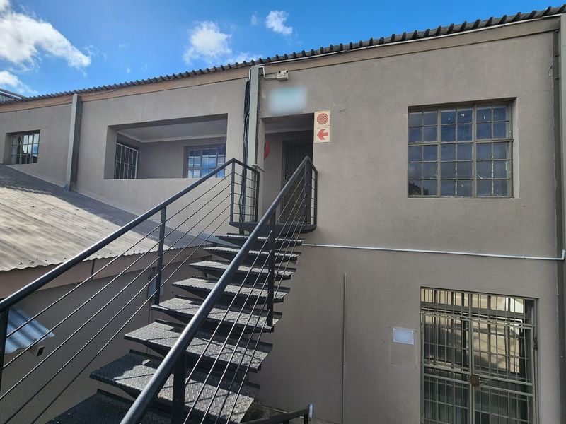 Rear exterior view of a commercial building featuring a metal staircase, security grilles on windows, and fire safety signage.