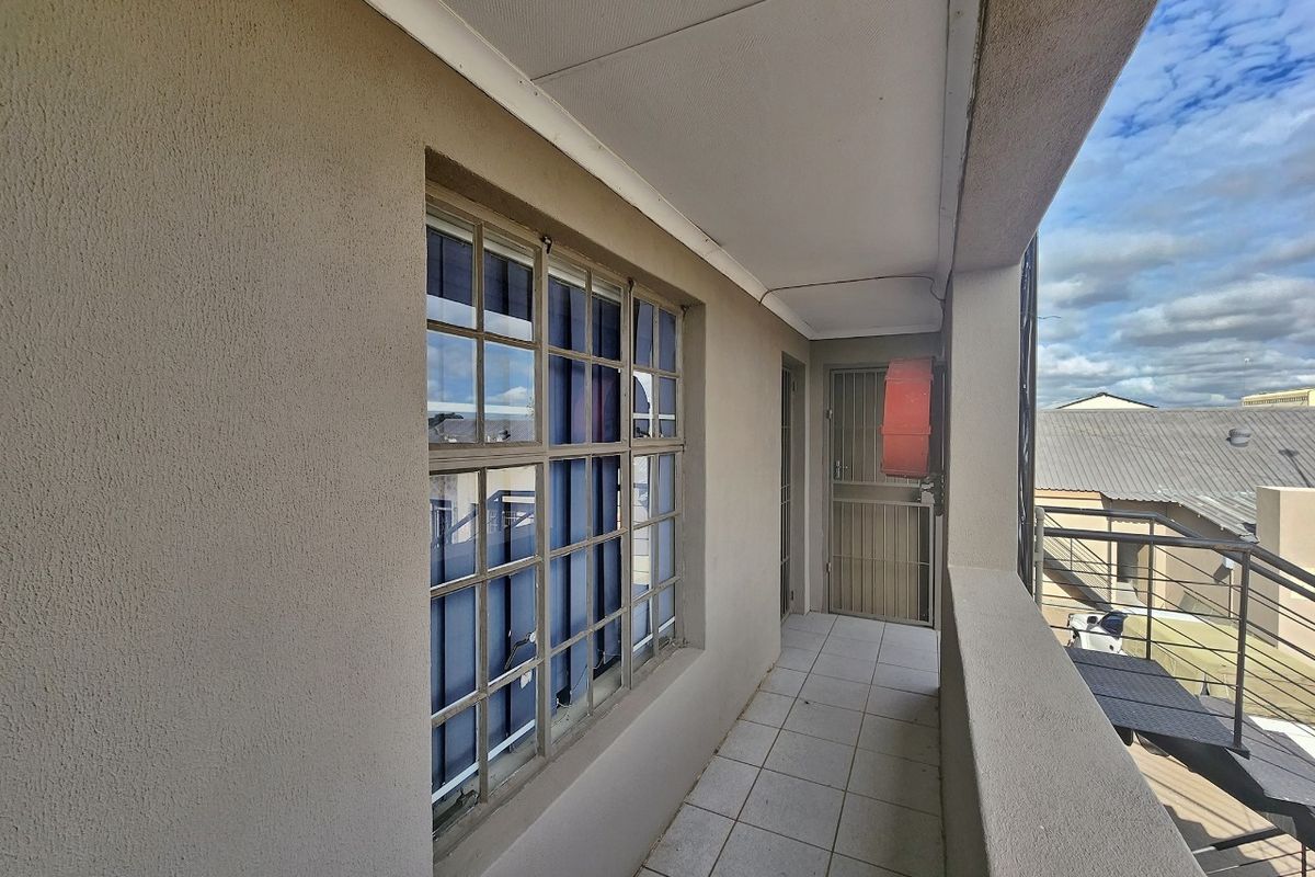 A covered exterior balcony featuring tiled flooring, a security gate, and a fire hose reel, providing access to the building's exterior.