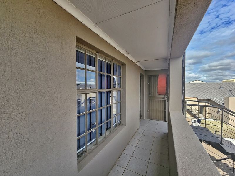 A covered exterior balcony featuring tiled flooring, a security gate, and a fire hose reel, providing access to the building's exterior.