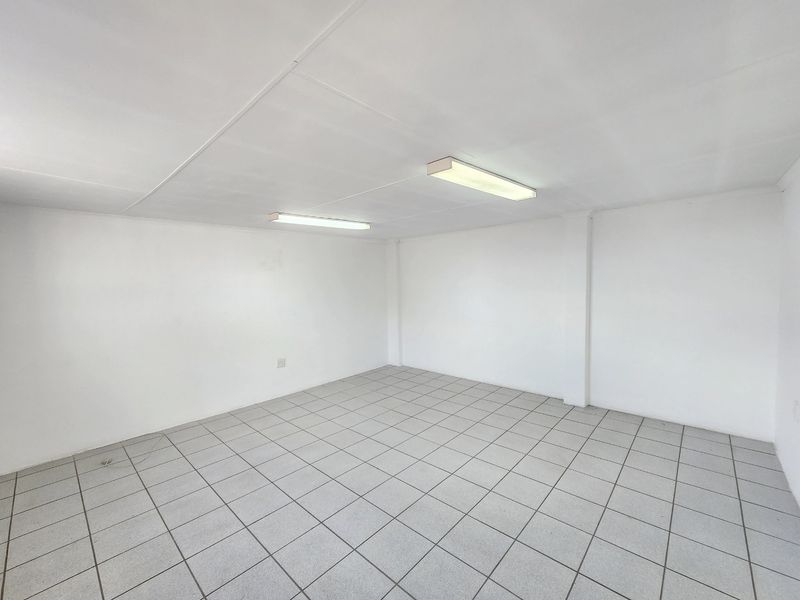 A clean, empty commercial office space featuring neutral tiled flooring and functional overhead fluorescent lighting, ready for immediate occupancy or custom fit-out.